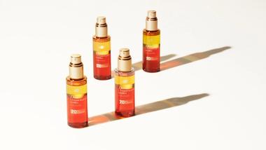 Four bottles of Dove’s UV Repair & Glow bi-phase serum to protect hair from UV damage. Glass bottles with orange and yellow serum.