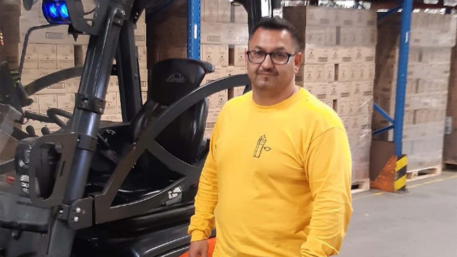 Image of Miltiatis standing in a warehouse next to his forklift truck