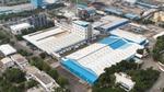 Aerial view of Unilever’s Gandhidham personal care site in India showing interconnected factory buildings with blue roofs, a central multi-storey processing unit with pipes and a chimney, loading bays, storage areas and access roads within a developed site.