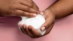 A closely cropped photo of a person in a pink top holding a Dove soap bar, with frothy white bubbles on their hands.
