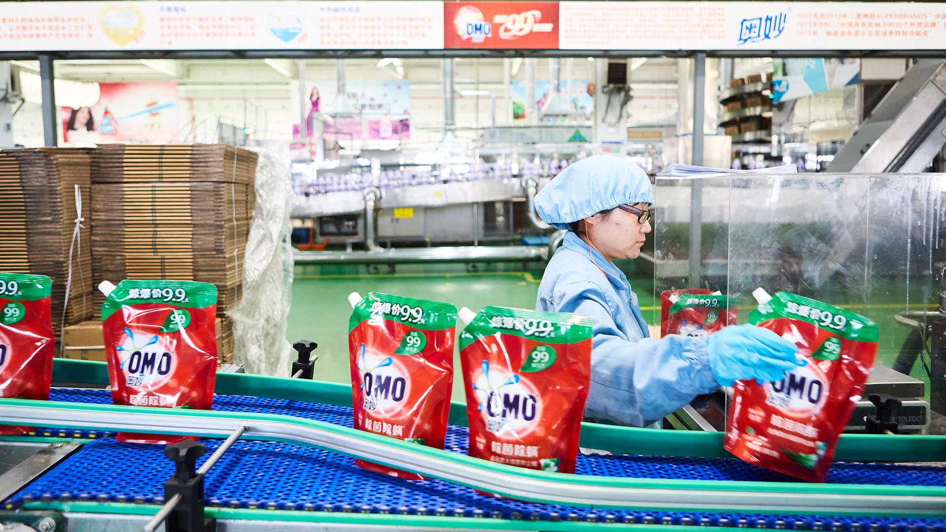 A lady wearing unilever uniform in a factory manning a line producing OMO laundry detergent