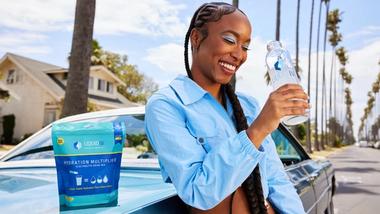 Woman standing by car drinking bottle of Liquid I.V. The product sits within Unilever’s Beauty & Wellbeing business group.