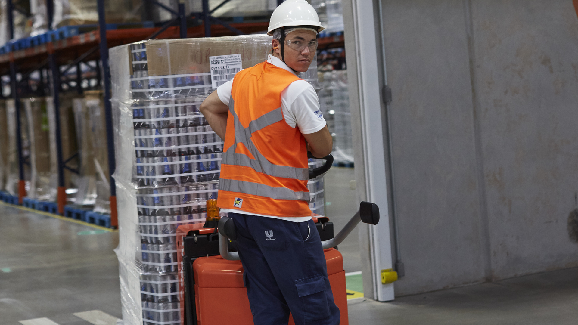 Worker in overalls and hard hat pulling a trolley across a factory floor