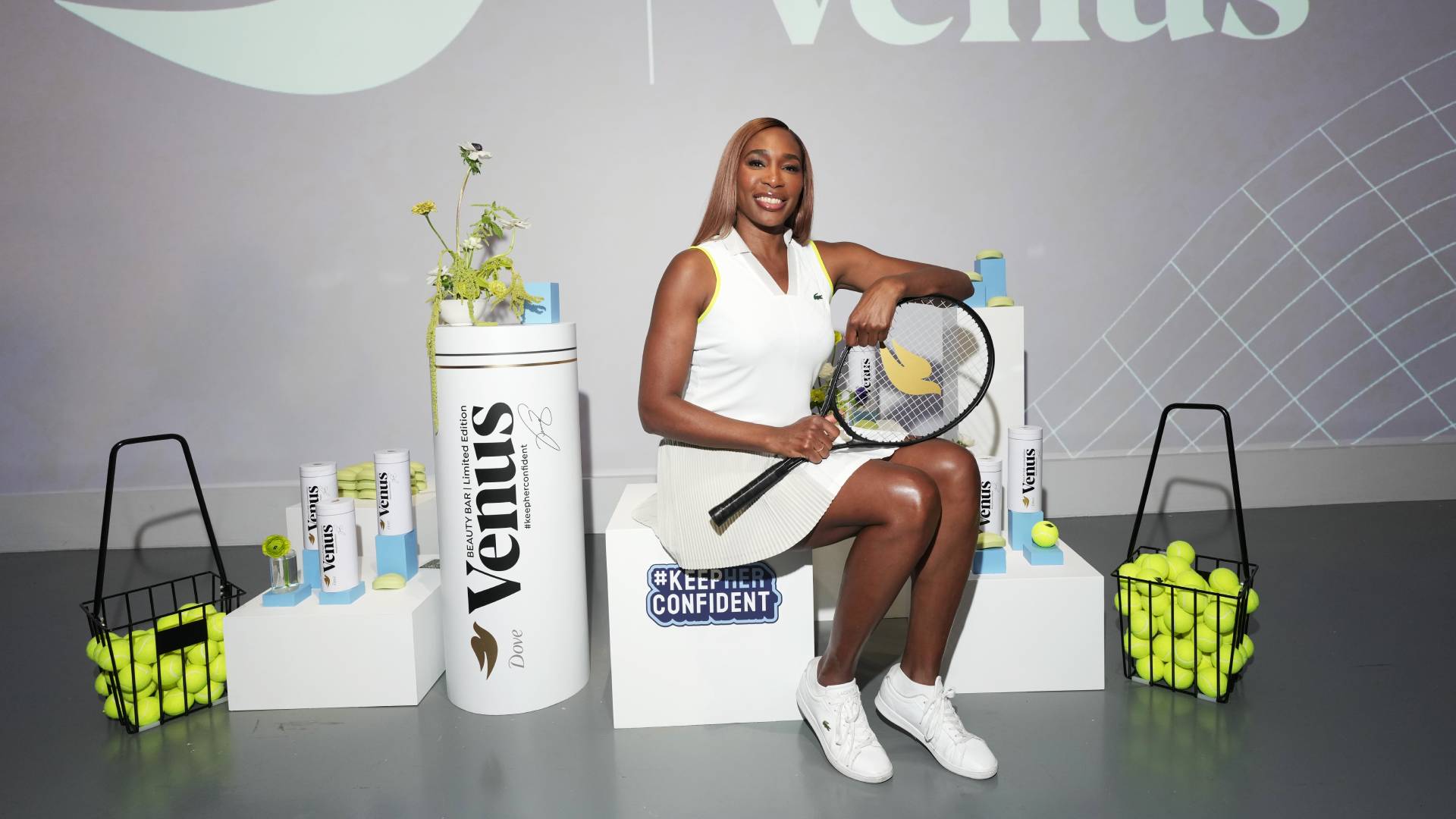 Tennis player Venus Williams at a Dove Keep her Confident launch event. Venus is sitting, holding a tennis racket and smiling at the camera.