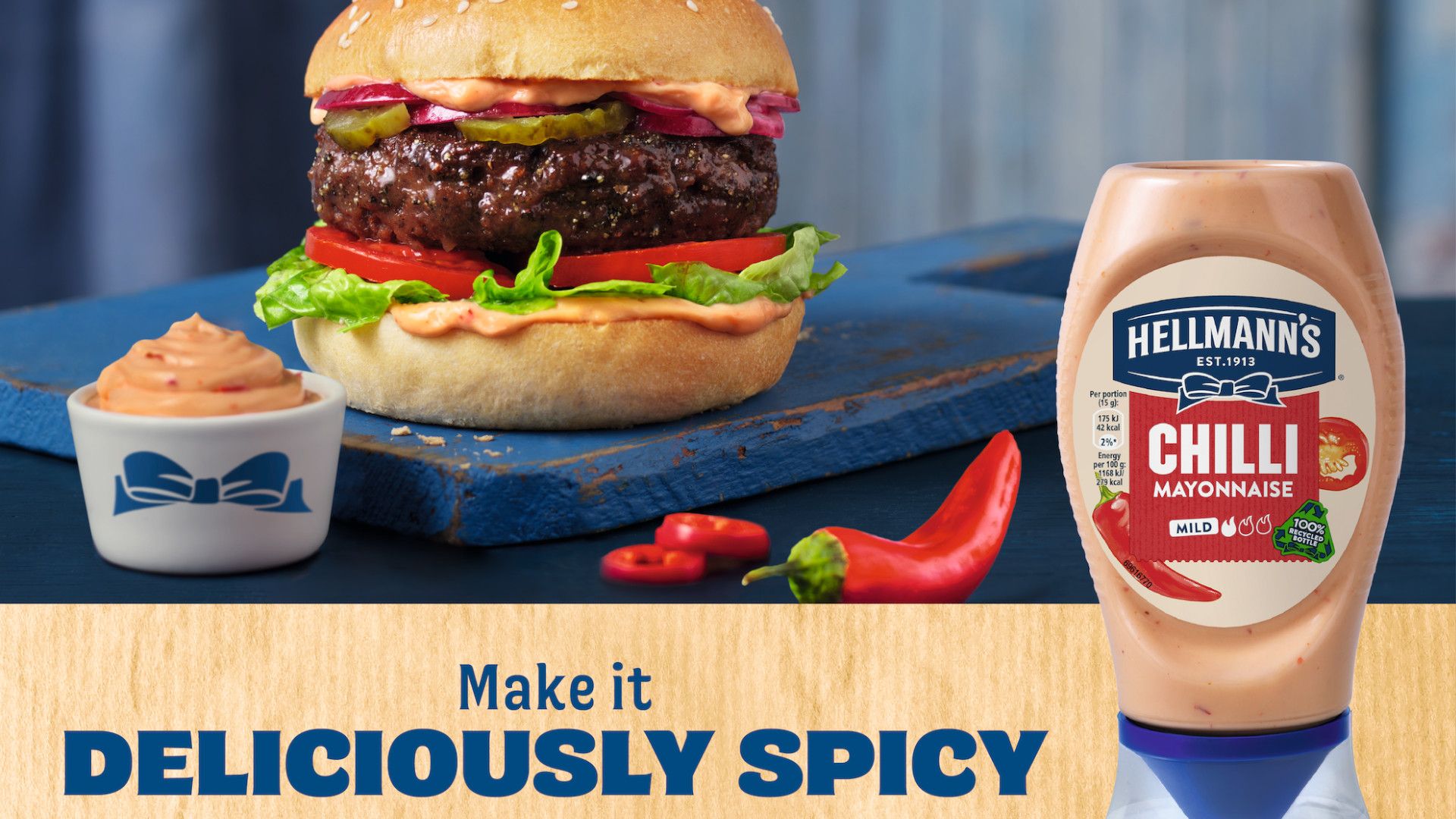 Image of a Hellmann’s chilli- flavoured mayo squeeze bottle in front of a fully loaded burger.