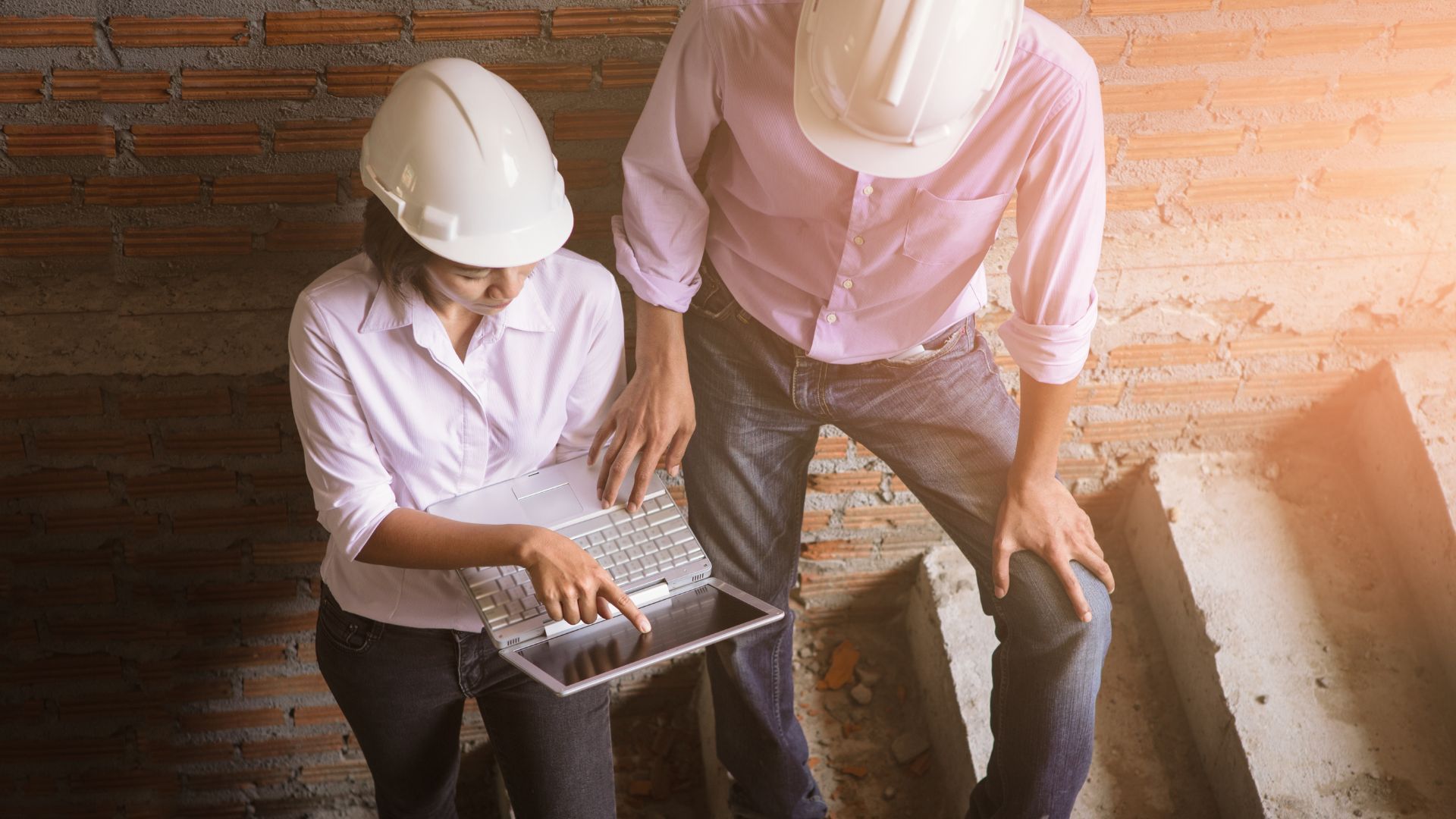 Two people in hard hats looking at a laptop