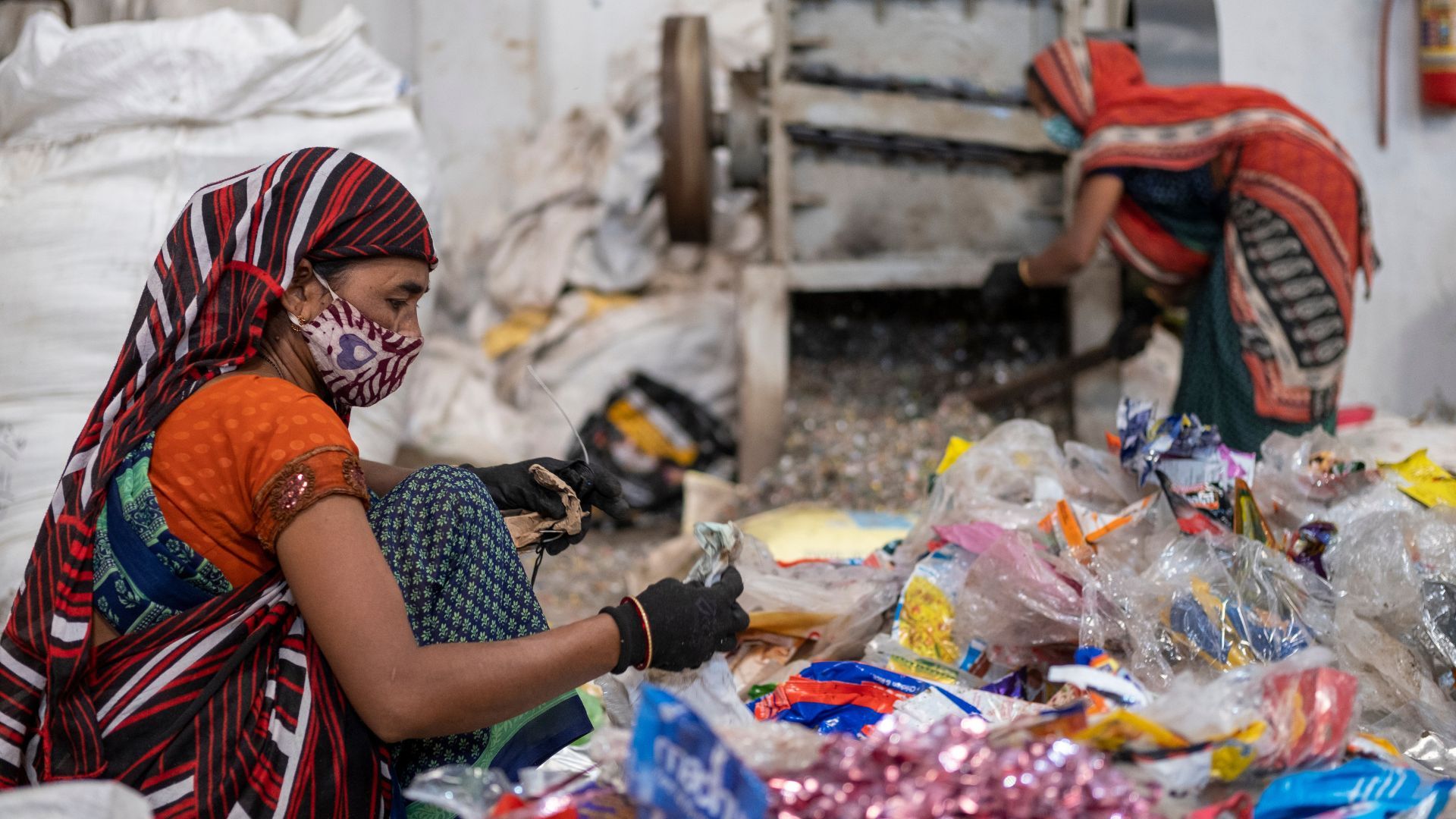 Two women wearing colourful saris and face masks, sorting through plastic waste.