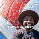 Elfried Samba wears a wide-brimmed hat standing in front of a large FIFA World Cup 2026™ football pop up.