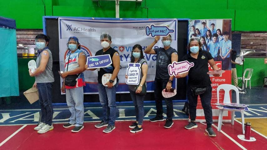 Group at vaccination centre, holding signs saying they have been vaccinated