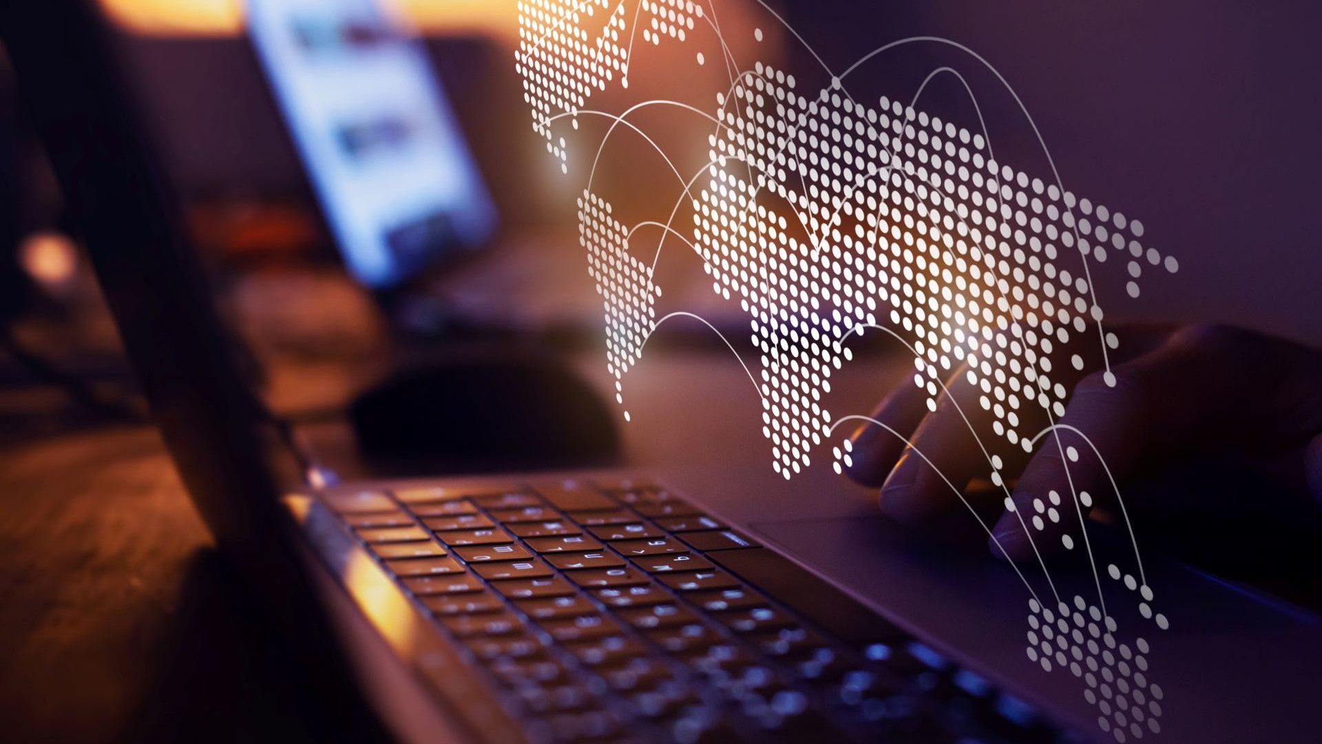 Close-up of a laptop keyboard with a digital world map overlay, featuring dotted continents and curved lines representing global connections, against a blurred background.