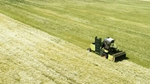 An agricultural machine harvesting crops in a large green field, with evenly cut rows stretching across the landscape.