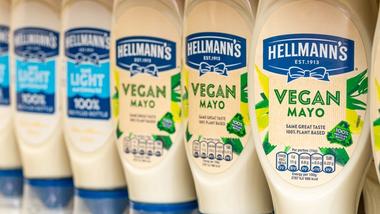 A close-up of Hellmann’s mayonnaise bottles on a shelf, featuring a mix of ‘Light’ and ‘Vegan Mayo’ varieties. The Vegan Mayo bottles are labelled with ‘Same Great Taste, 100% Plant-Based’ and ‘100% Recycled Bottle’.