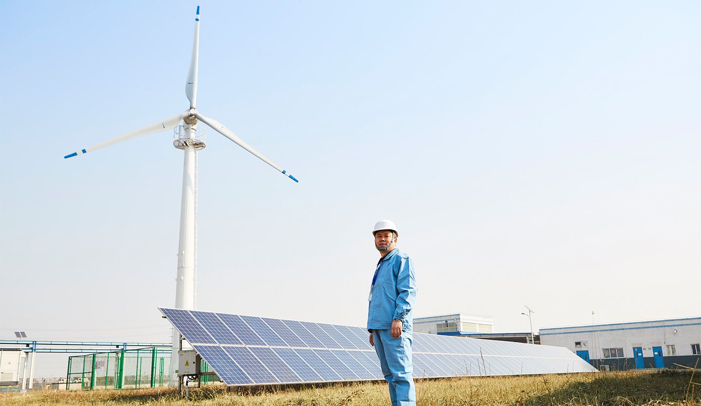 Worker in front of solar panels and wind turbine