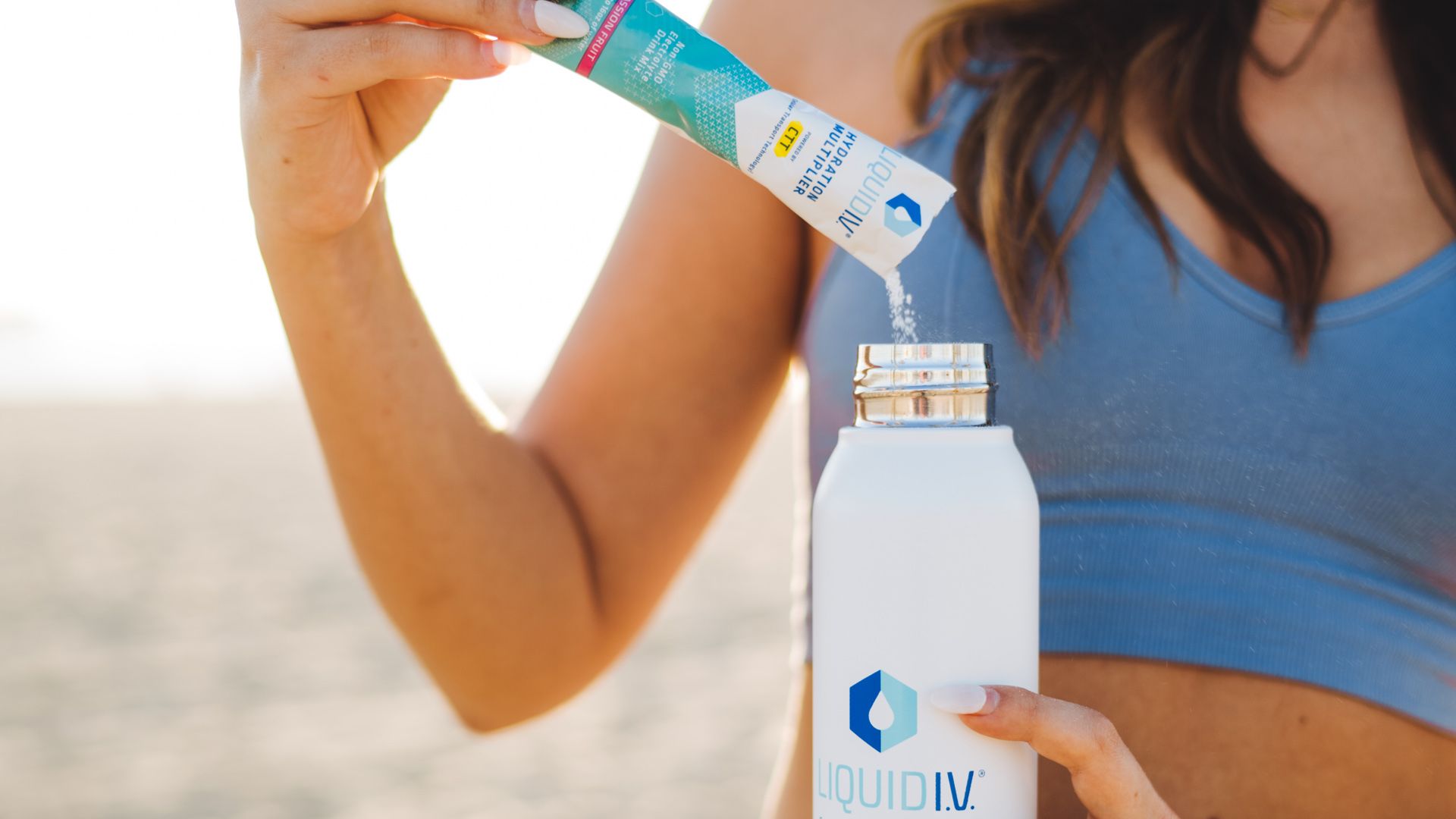Woman pouring powdered Liquid I.V. electrolyte drink mix from a sachet into a bottle.