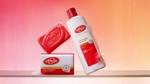 New red Lifebuoy soap bar and a new Lifebuoy body wash in a white, red and gold bottle. Background is pink and orange.