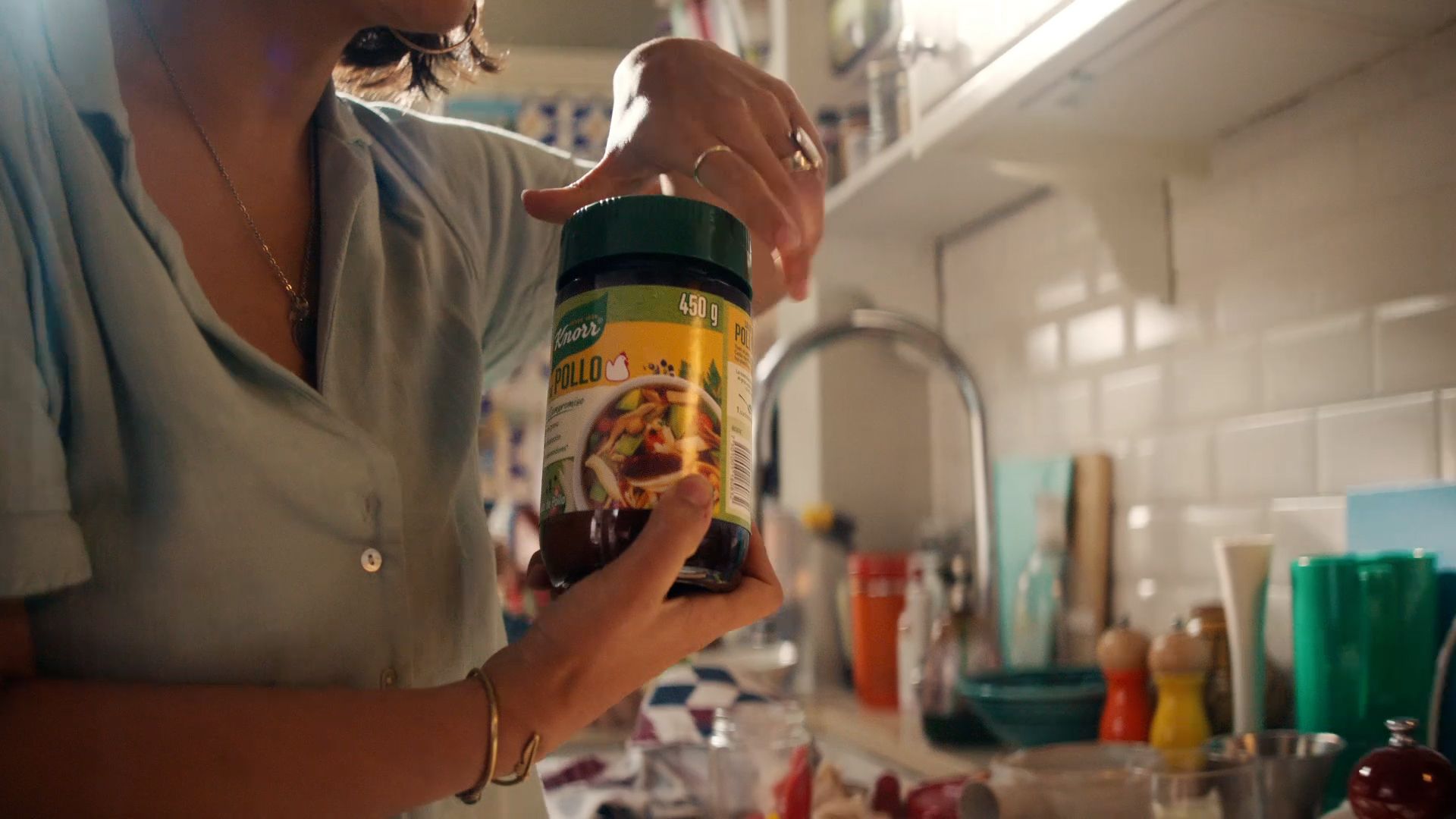 A woman opening a jar of chicken bouillon in a light-filled kitchen