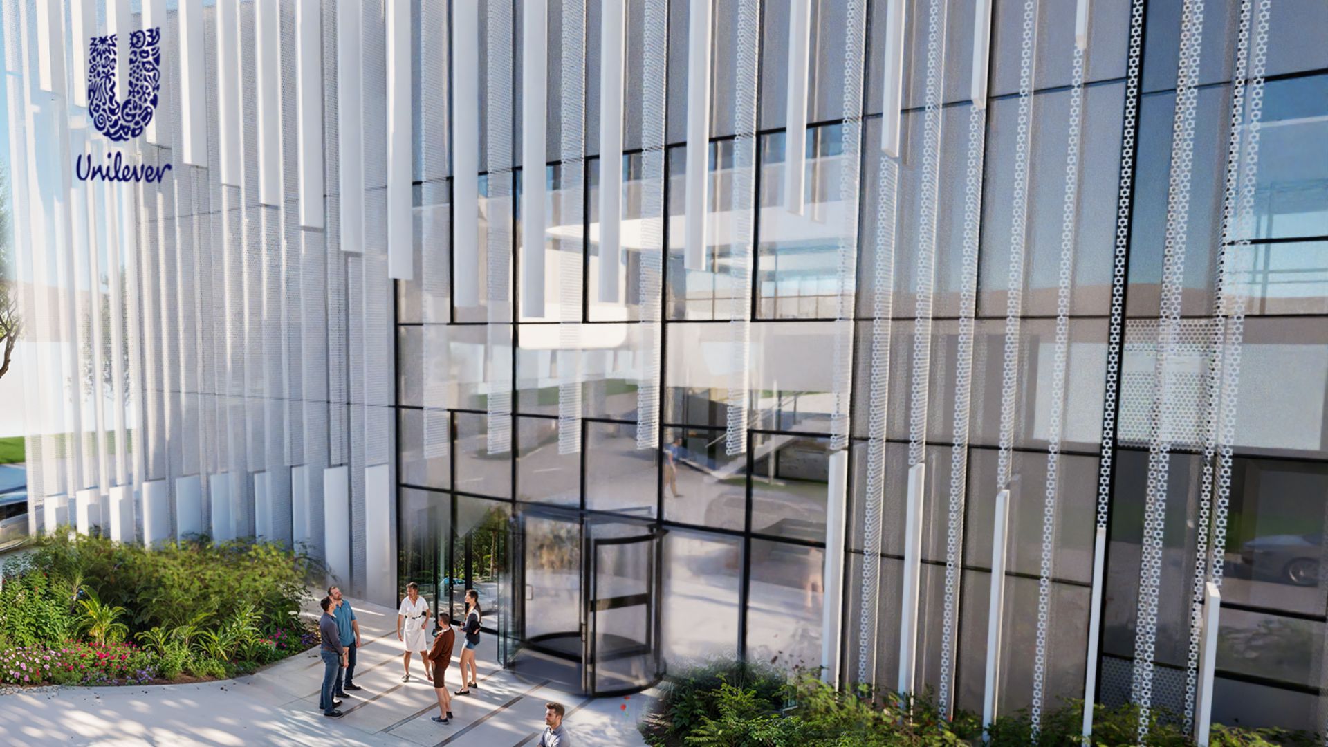 An artist’s impression of a modern office building with a glass facade and vertical white slats. The Unilever logo is visible in the top left corner. Several people are walking or standing near the entrance, which features revolving doors. The surrounding area has landscaped greenery and flowers.