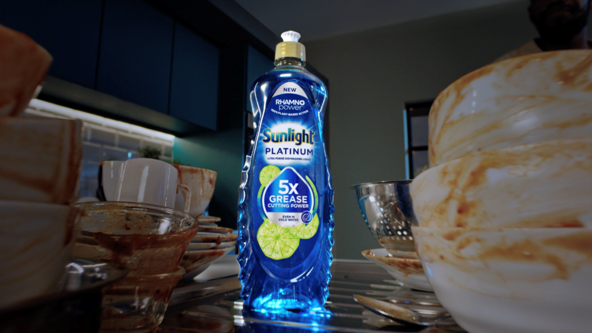 A bottle of Sunlight Platinum dishwashing liquid stands among dirty dishes, highlighting its 5x grease-cutting power.