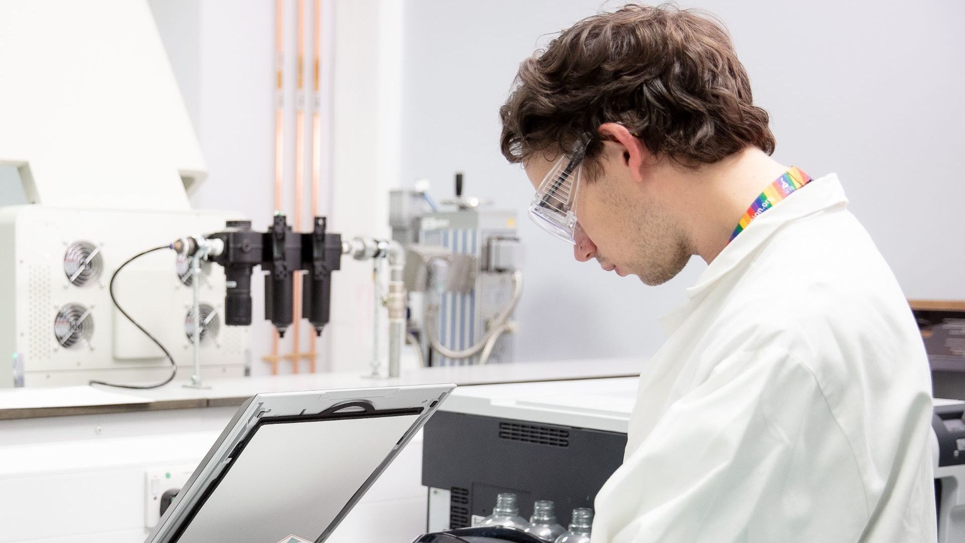 A scientist in a white coat and safety goggles using laboratory equipment in a modern research facility.