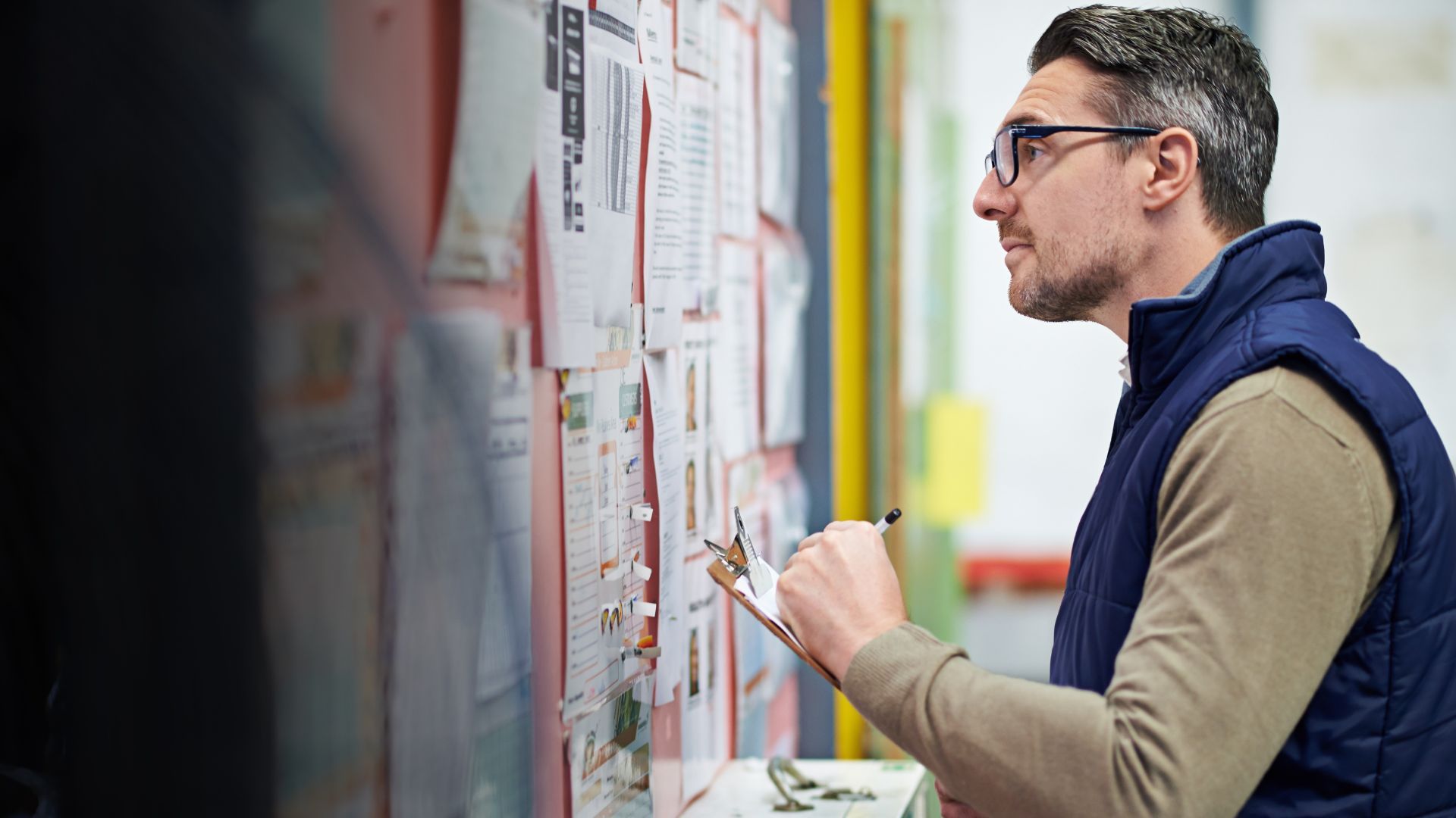 Man with glasses looking closely at a noticeboard.