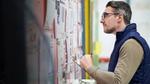 Man with glasses looking closely at a noticeboard.