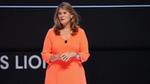 Conny Braams in an orange dress speaking on stage
