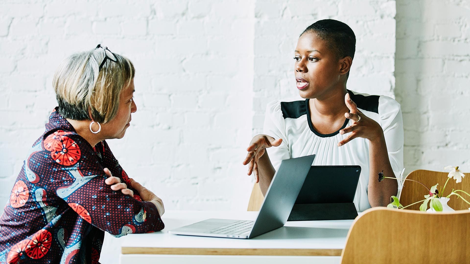 Two women in animated discussion over their laptops
