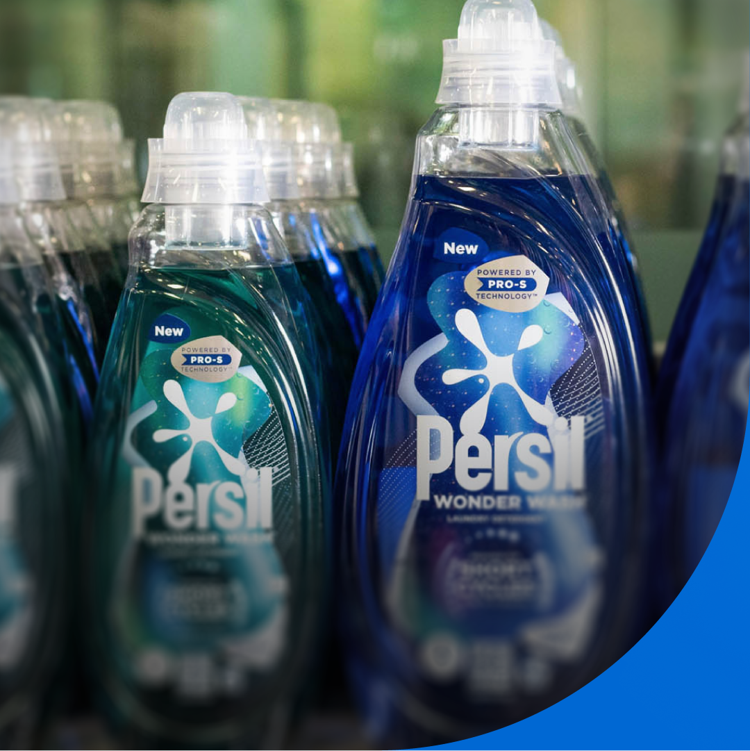 A close-up view of several plastic bottles of Persil Wonder Wash liquid detergent arranged in rows on a shelf. 