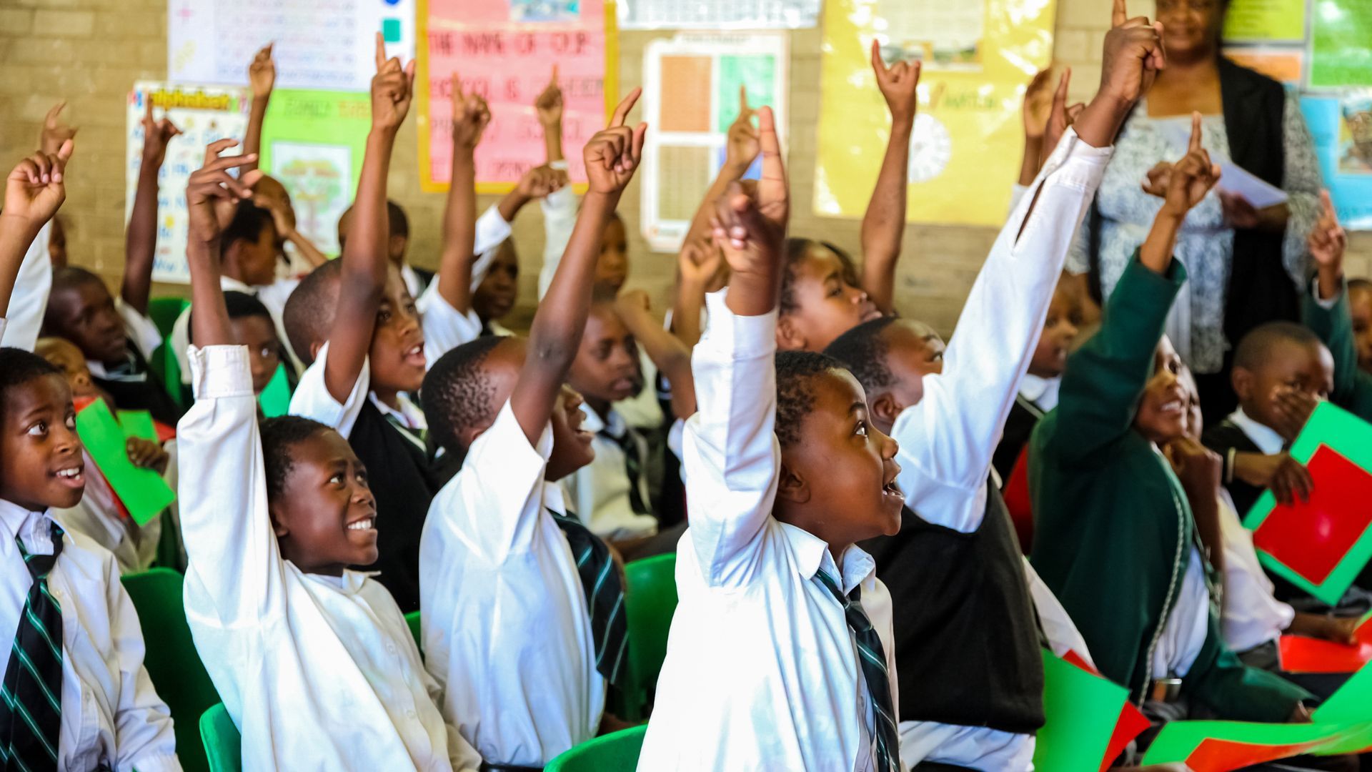 Children wearing their school uniforms eagerly holding up their hands to answer a question