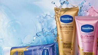 Three Vaseline Healthy Bright Gluta-Hya serum burst lotion tubes in gold, pink, and purple displayed against a water splash background.
