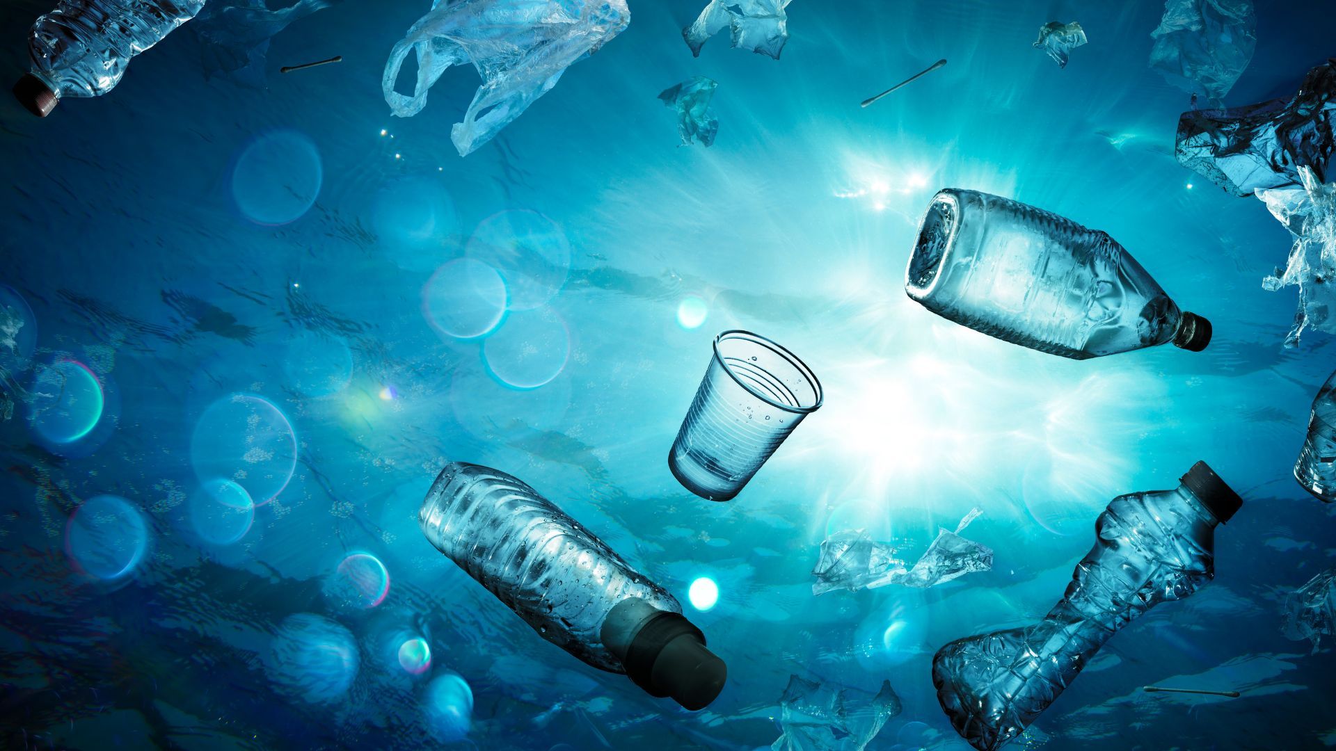 Underwater perspective of various plastic bottles, cups and shopping bags floating in the sea.