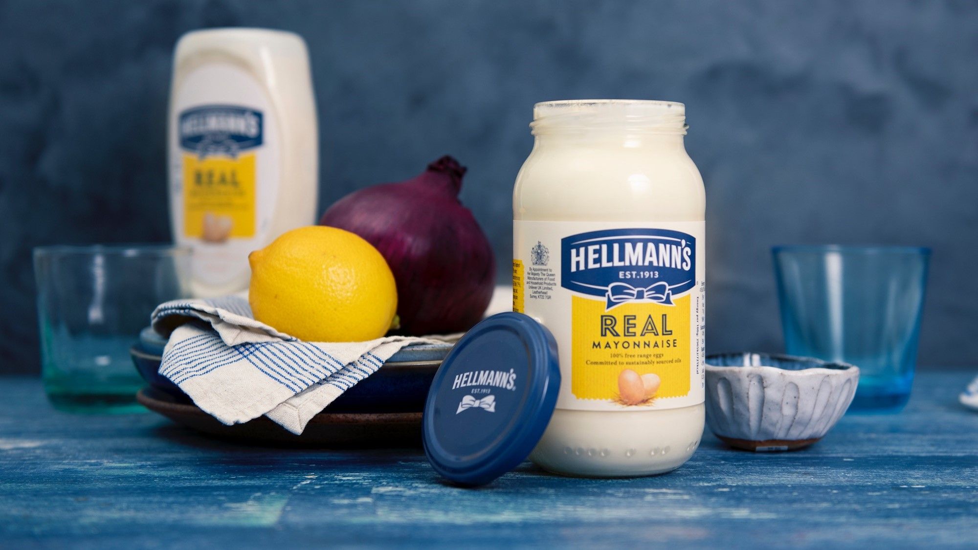 A jar of Hellmann's mayonnaise with other food ingredients in the background.