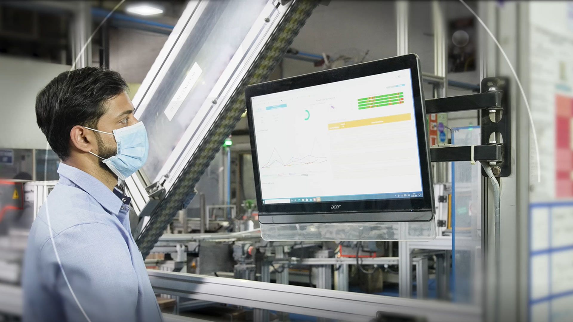 Man in front of two computer screens with a factory setting blurred in the background