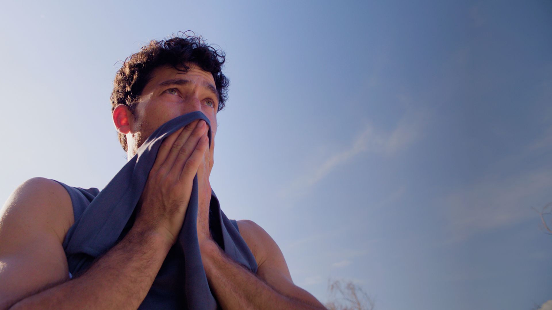 Close-up of a person outdoors holding a towel to their face under a clear blue sky.