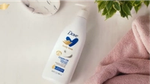 Dove Body Love Cream Oil lotion bottle beside pink towels and green leaves.