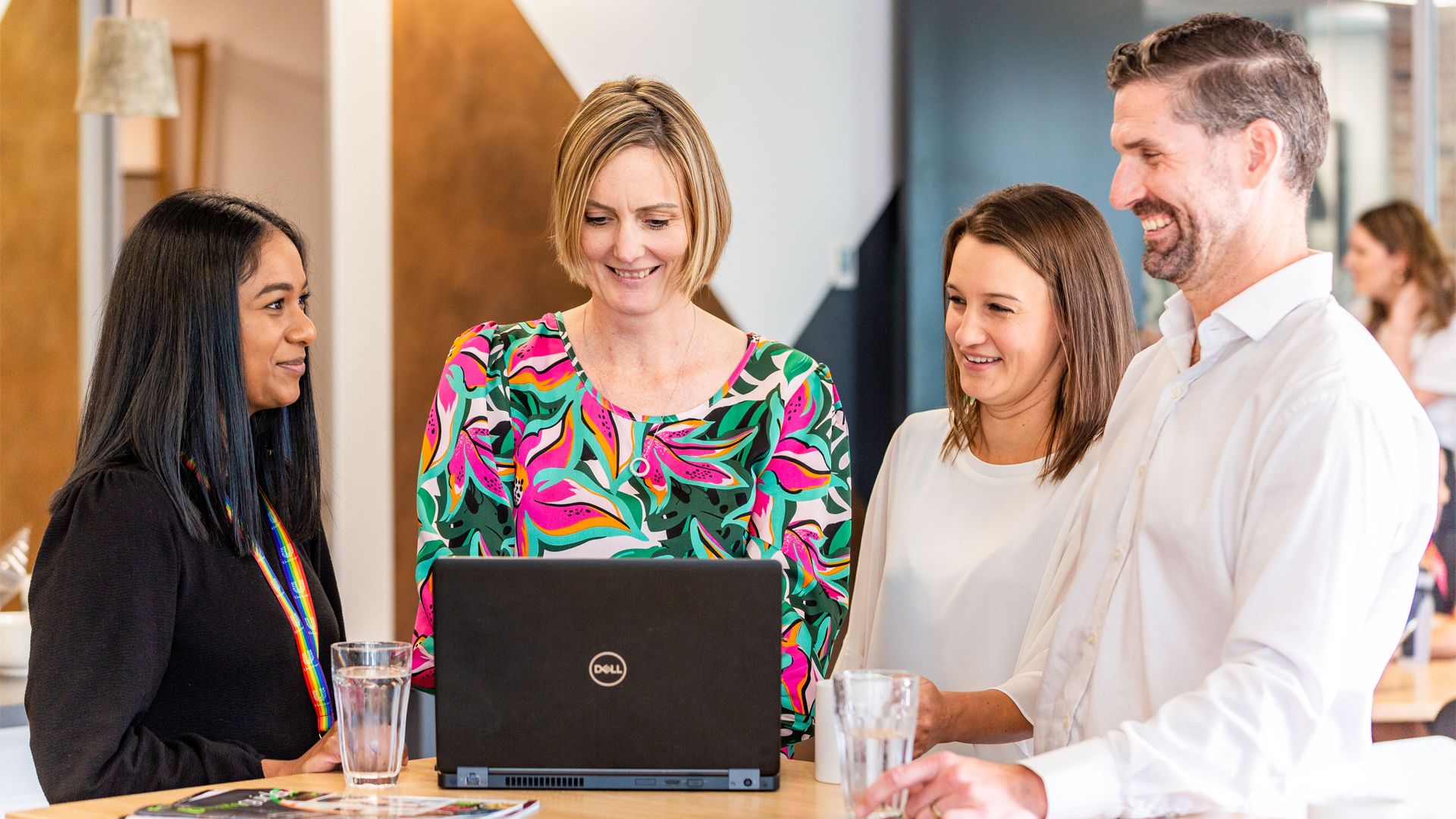 Four employees gathered round a table with a laptop, looking happy and engaged