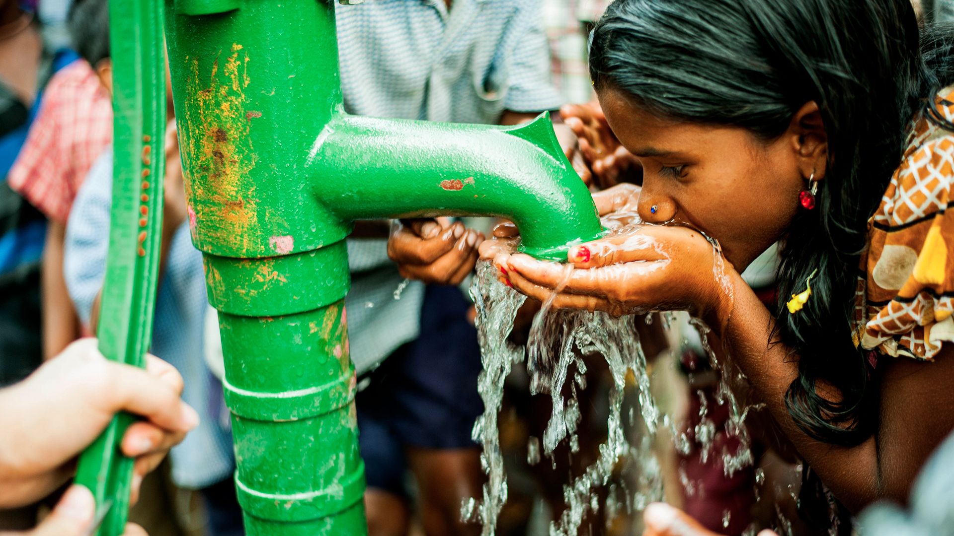 Girl cupping her hands and drinking clean, safe water from a community tap 
