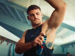 A man dressed for the gym confidently applies deodorant to his underarm.
