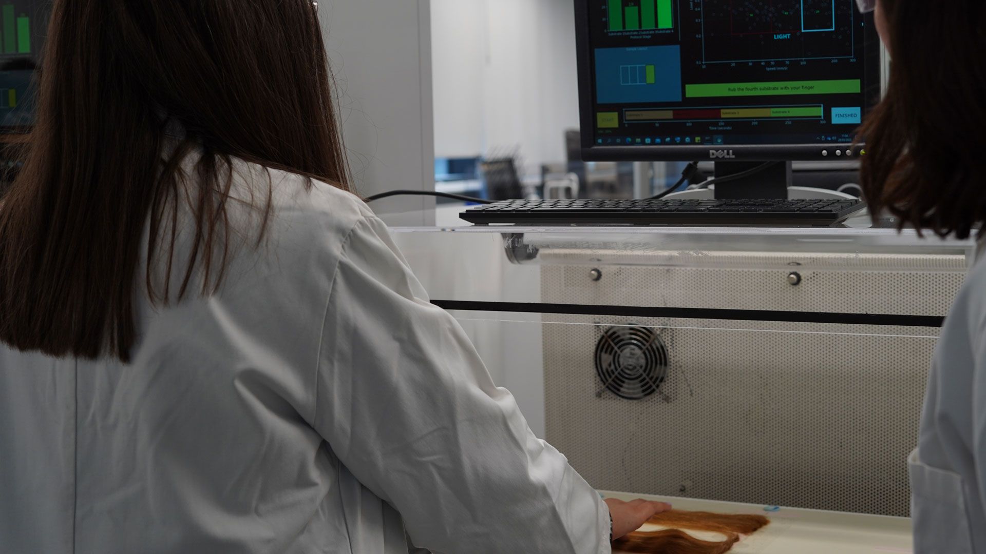 A Unilever scientist with long brown hair examines hair samples prepared by a robot at the Materials Innovation Factory