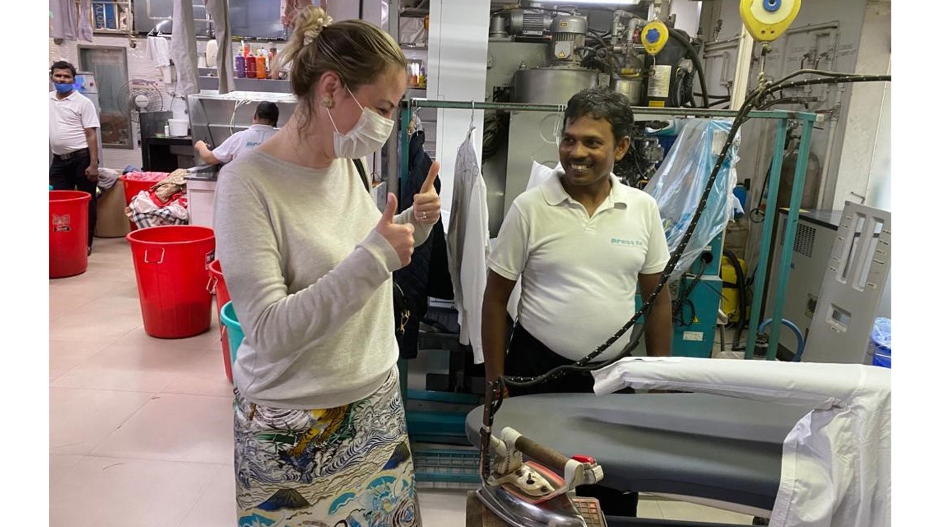 Deniz speaking to a man next to an ironing board