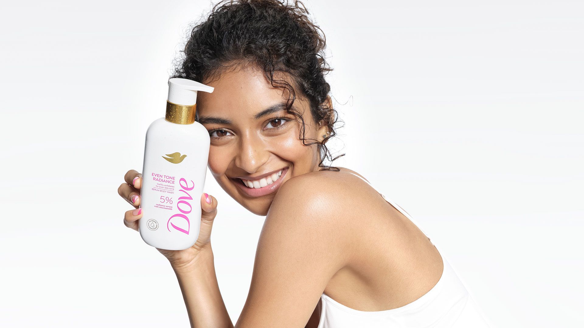 A person holding a Dove moisturising body lotion bottle with gold accents, shown against a bright, clean background. 