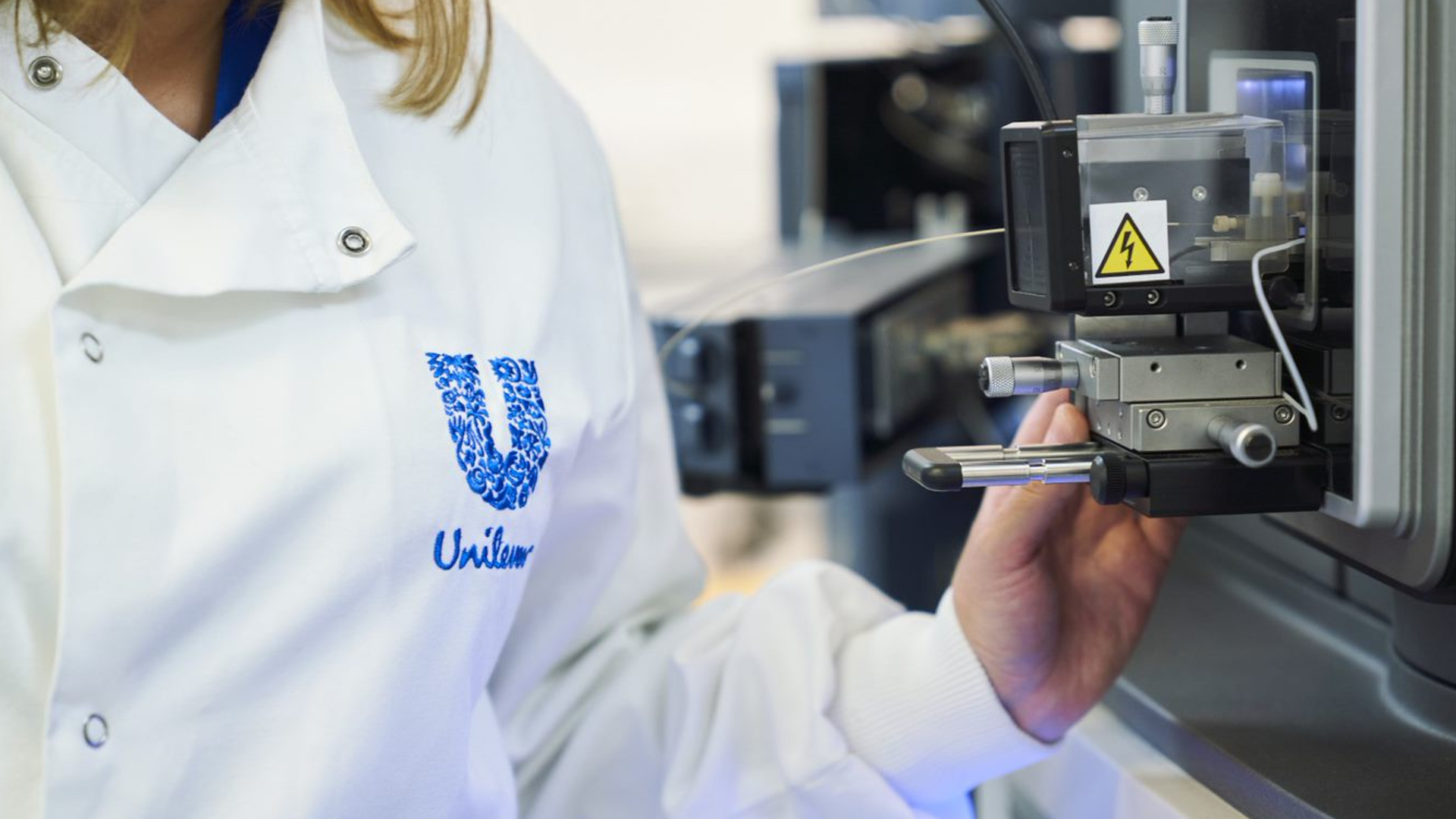  A close-up photo of a scientist wearing a white lab coat with a Unilever logo on the chest.