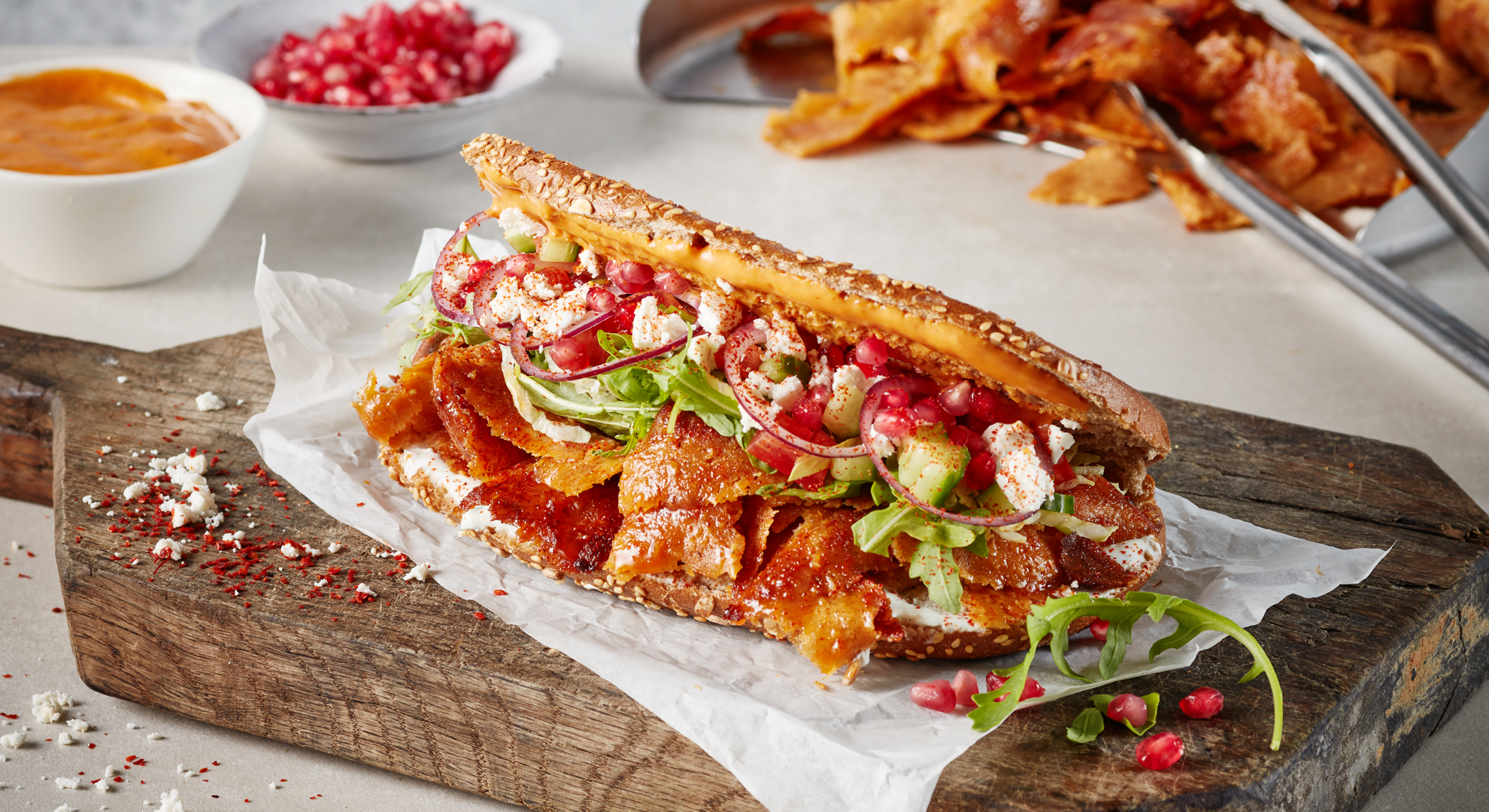 : A plant-based döner kebab on a wooden chopping board with relish and a dish of kebab pieces in the background