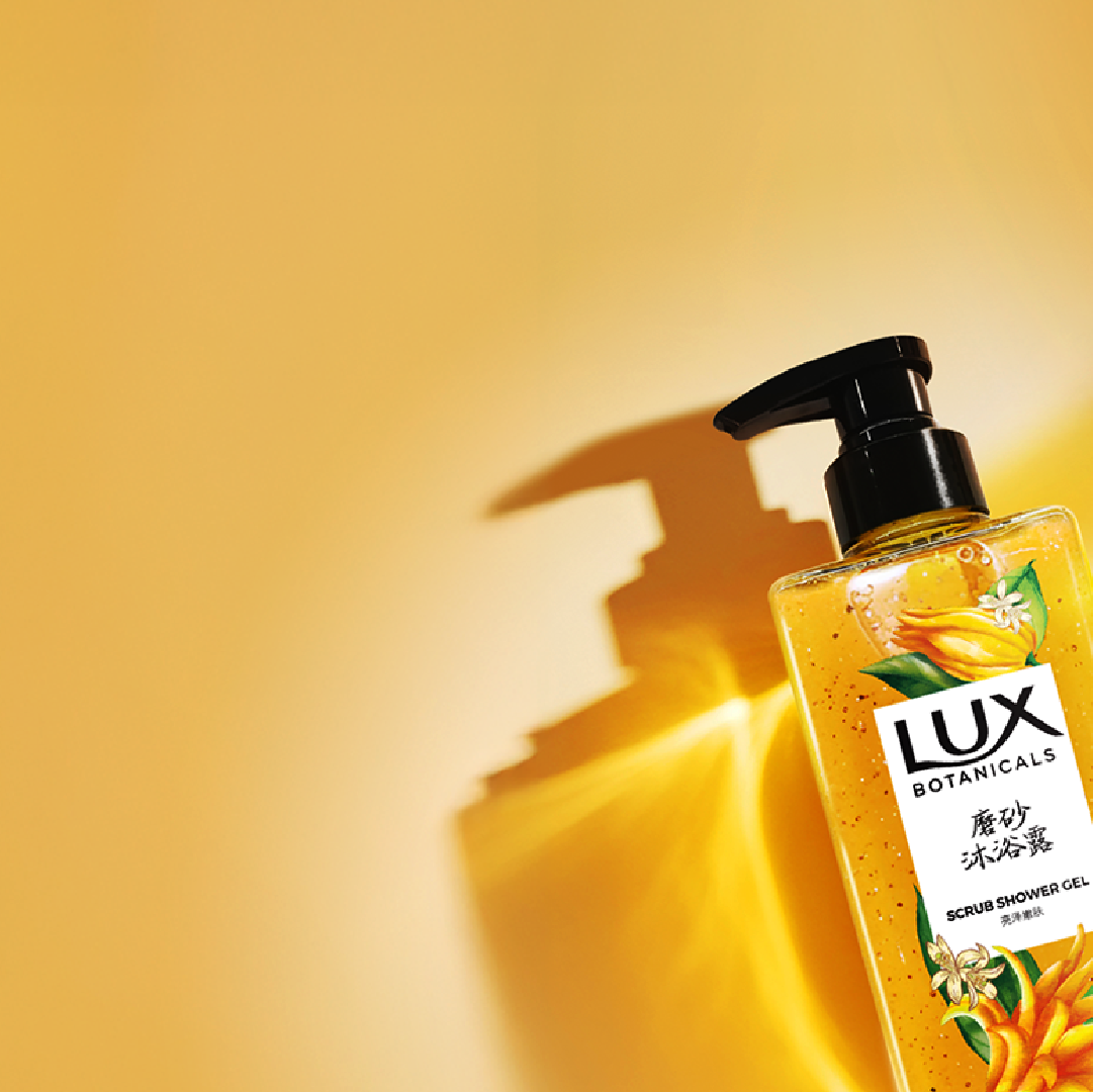 Lux Botanicals Scrub Shower Gel bottle on yellow background.