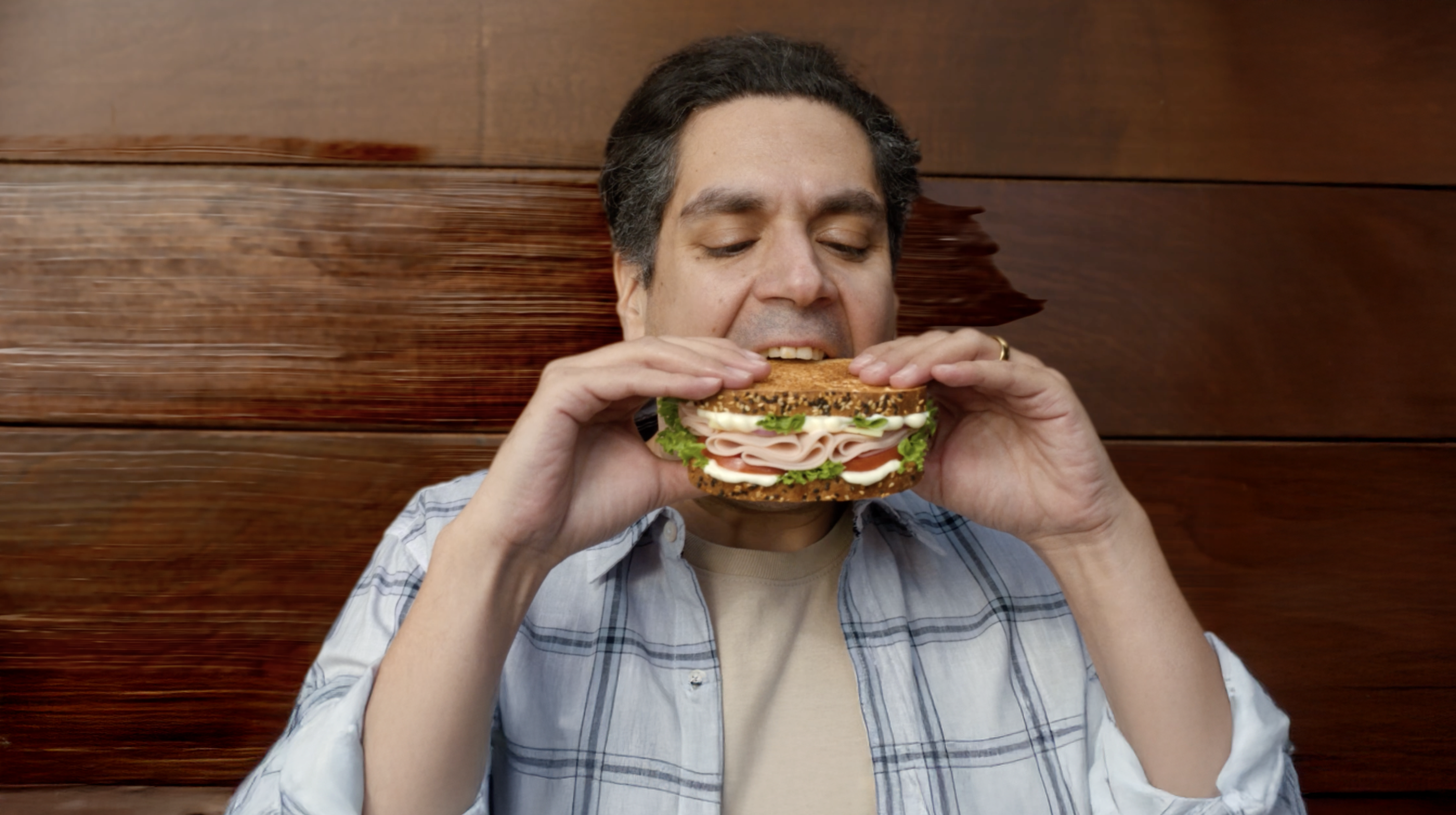 A man prepares to take a bite from a huge ham salad sandwich with mayonnaise.