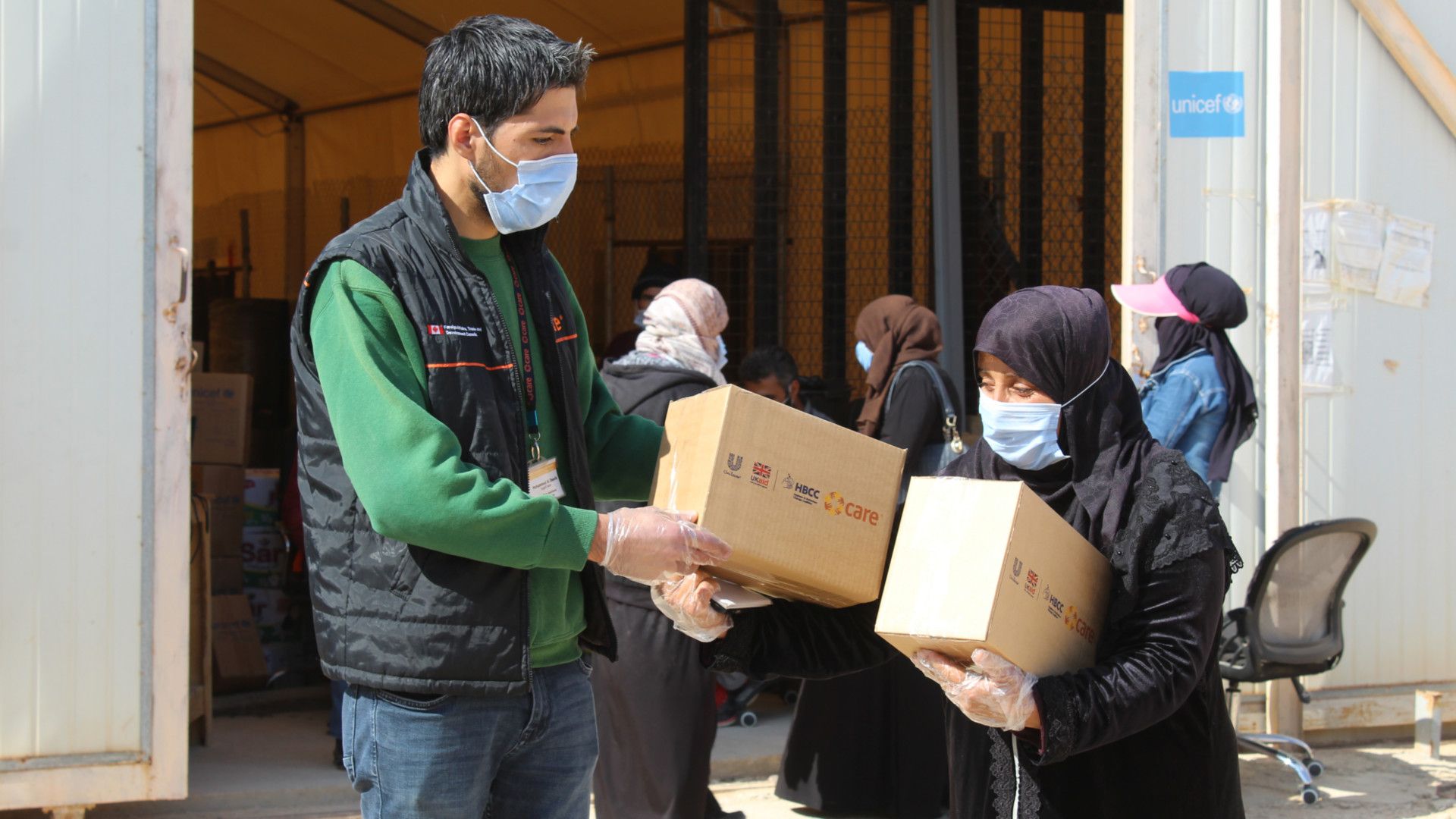 Aid worker wearing a mask giving boxes of Unilever hygiene products to a woman wearing a mask in Jordan