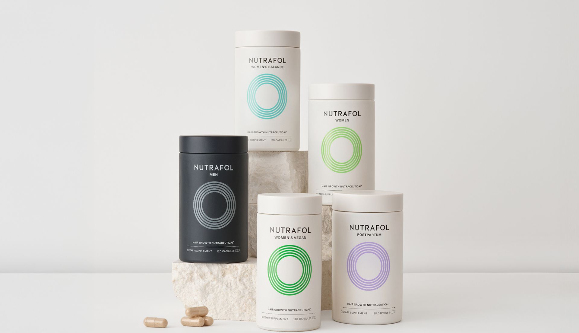 Collection of Nutrafol hair growth supplement containers arranged on stone blocks, featuring variants for men and women.