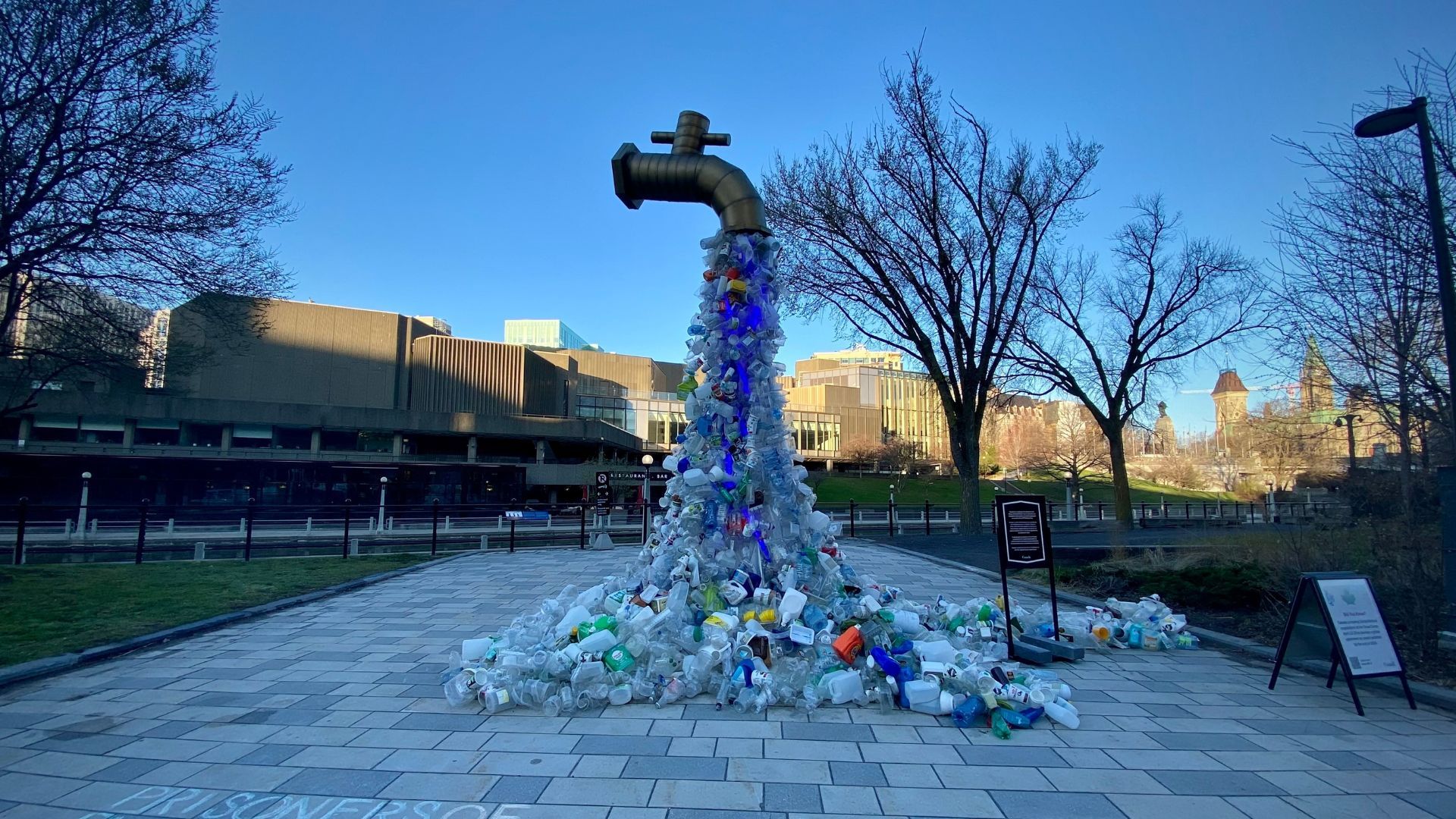Large sculpture of a tap with plastic waste flowing out of it and pooling on the ground.