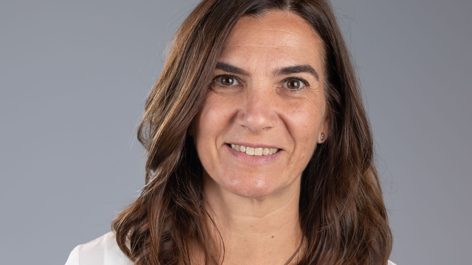 Unilever’s Nuria Hernadez-Crespo. Nuria is white with shoulder-length brown hair. She is wearing a white shirt and smiling.