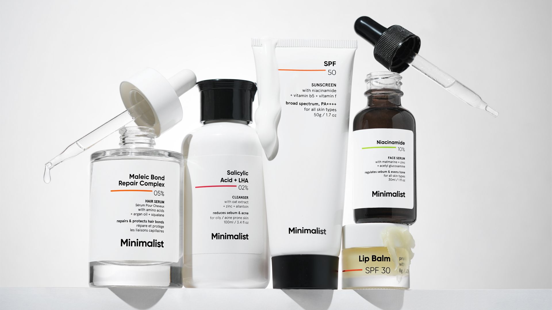 A variety of Minimalist products – a clear glass jar with a dropper, a white plastic bottle with a black lid, a white plastic tube with a black lid, a brown glass bottle with a dropper and a small tub.